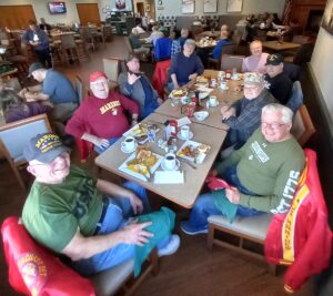 Eight members of Marine Corps League Seacoast Detachment sit around a diner table eating breakfast together.