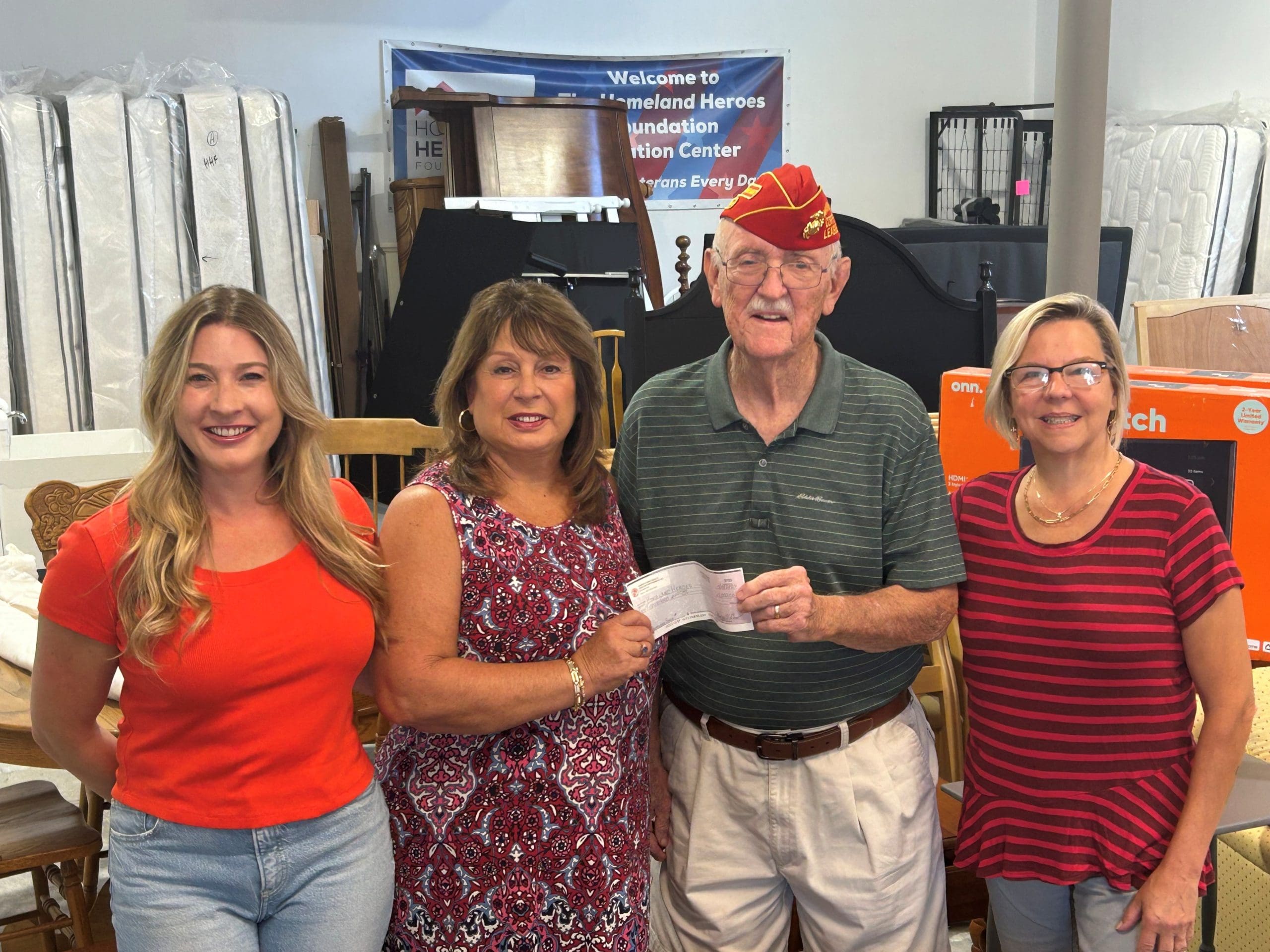 Marine Corps League member in his red cover gives donation check to three ladies from Homeland Heroes Foundation.